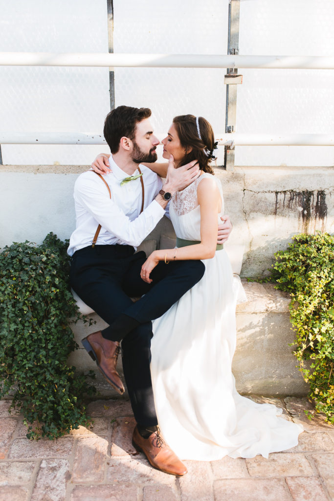Brautpaar sitzt auf einer Mauer und küsst sich fast