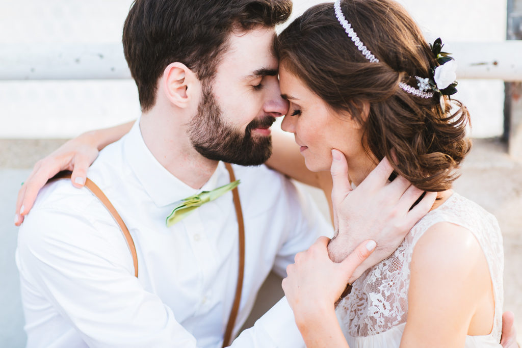 Brautpaar lehnt mit Stirn aneinander, Braut hält Arm des Bräutigams fest