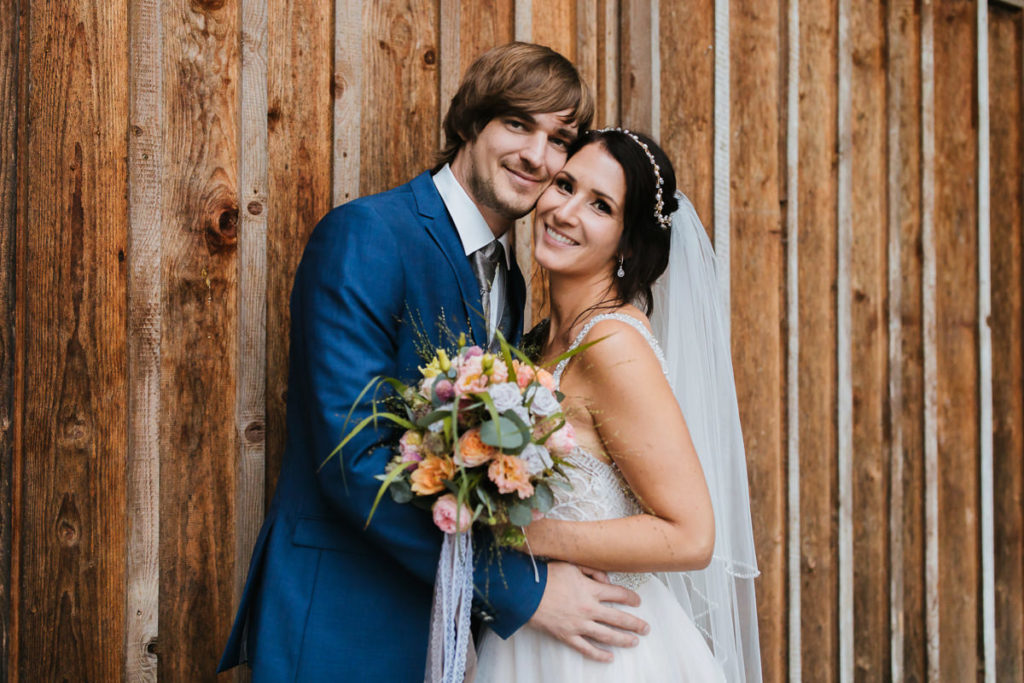 Brautpaar lacht in die Kamera vor Scheunenwand